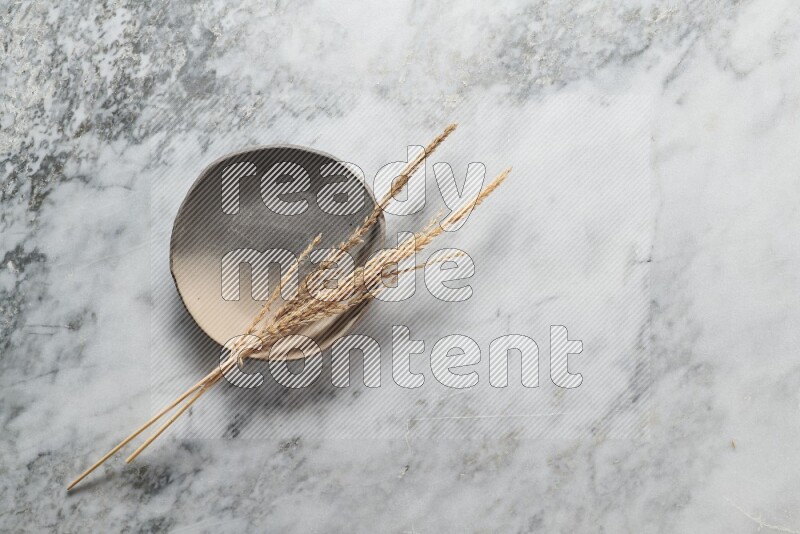 Wheat stalks on multicolored pottery plate on grey marble background