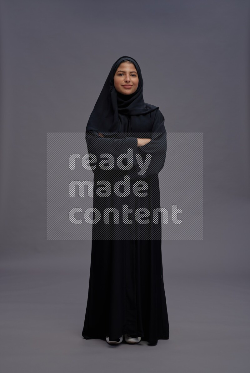 Saudi woman wearing Abaya standing with crossed arms on gray background
