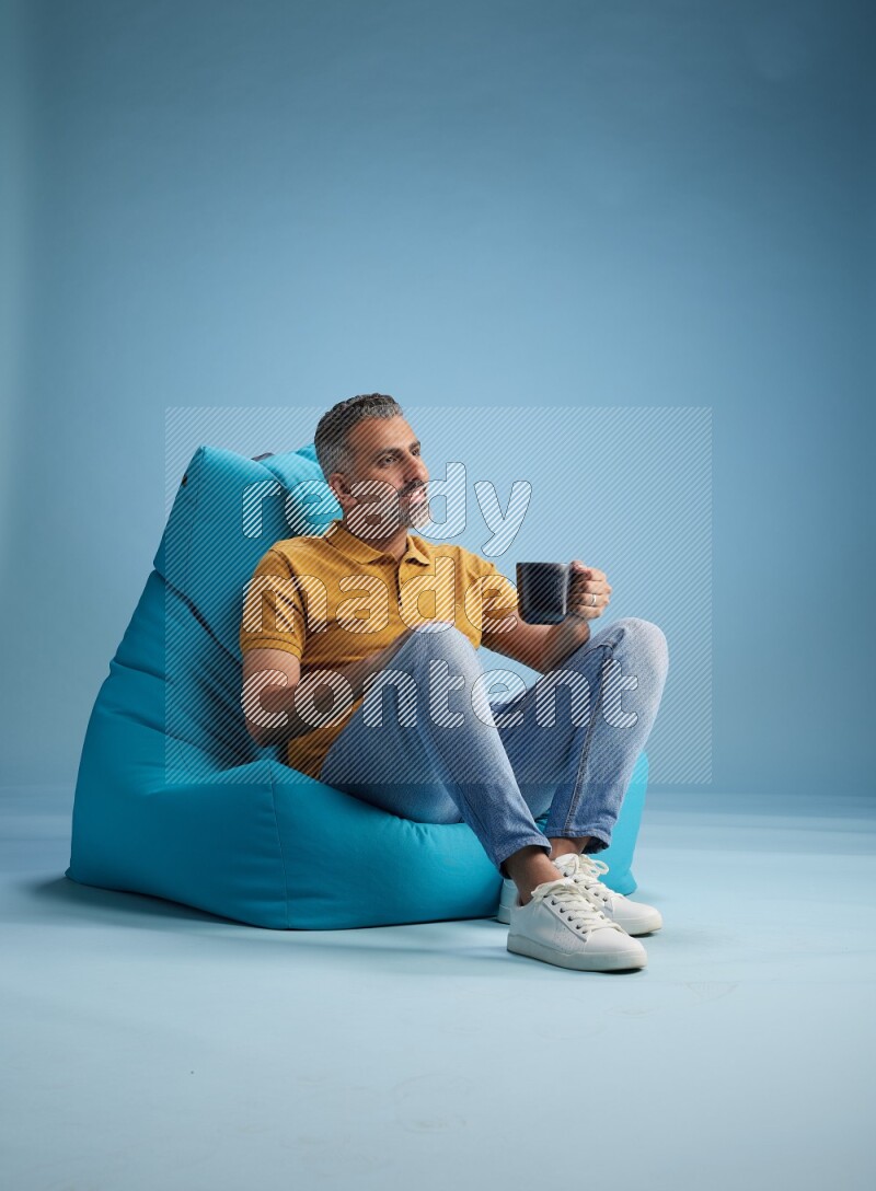 A man sitting on a blue beanbag and drinking coffee