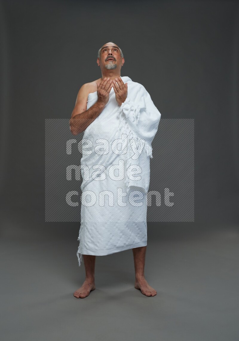 A man wearing Ehram Standing dua'a on gray background