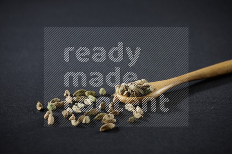 A wooden spoon full of cardamom on black flooring