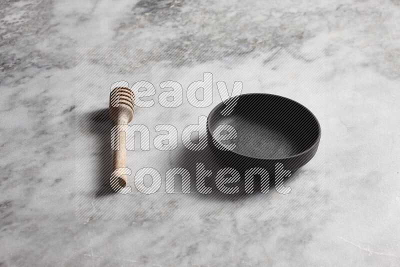 Black pottery bowl with wooden honey dipper on the side on grey marble background