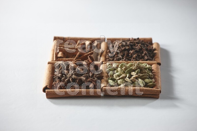 4 مربعات من أعواد القرفة ممتلئة بالهيل واليانسون النجمي والقرنفل والقرفة على أرضية بيضاء