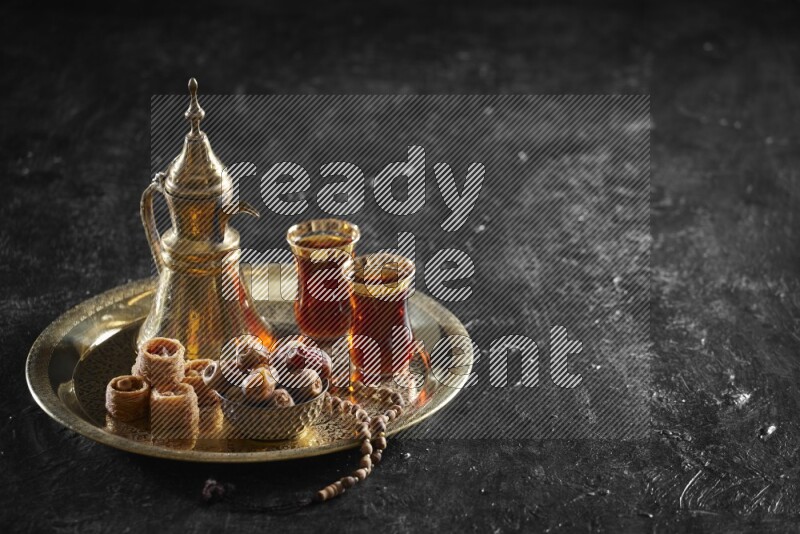 Oriental sweets with dates and a drink on a metal tray in a dark setup