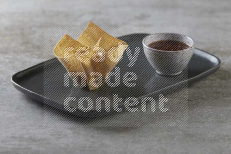 wonton cups with soy sauce ramkin on rectangle dark grey ceramic plate on grey textured counter top