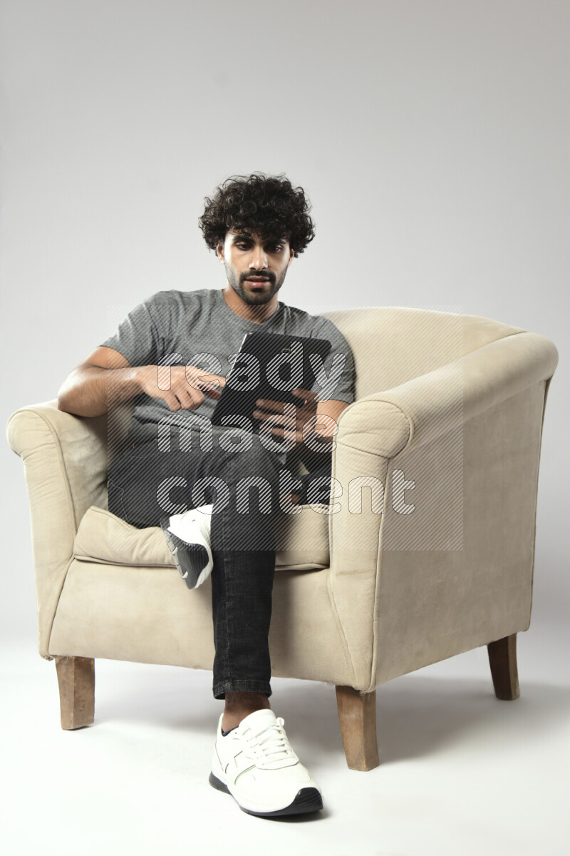 A man wearing casual sitting on a chair browsing on a tablet on white background
