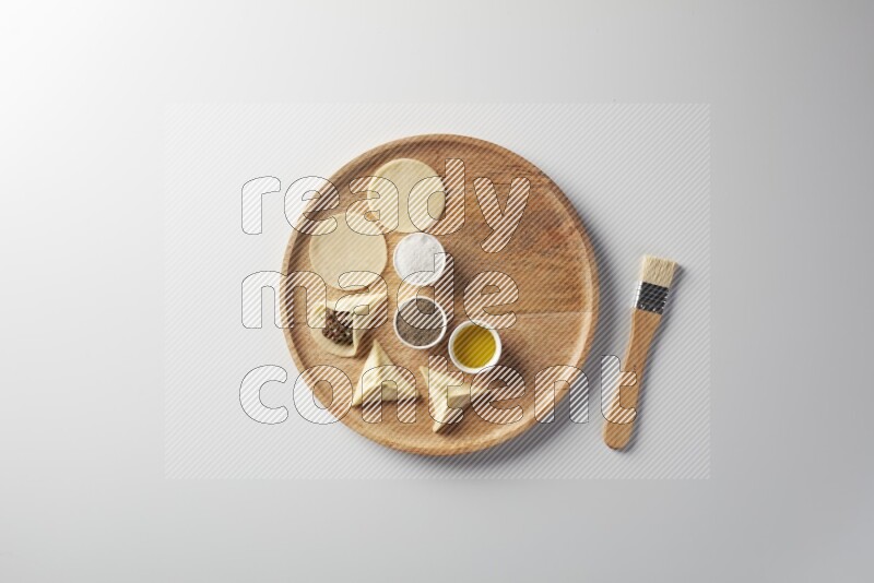 two closed sambosas and one open sambosa filled with meat while salt, black pepper and oil with oil brush aside in a wooden dish on a white background