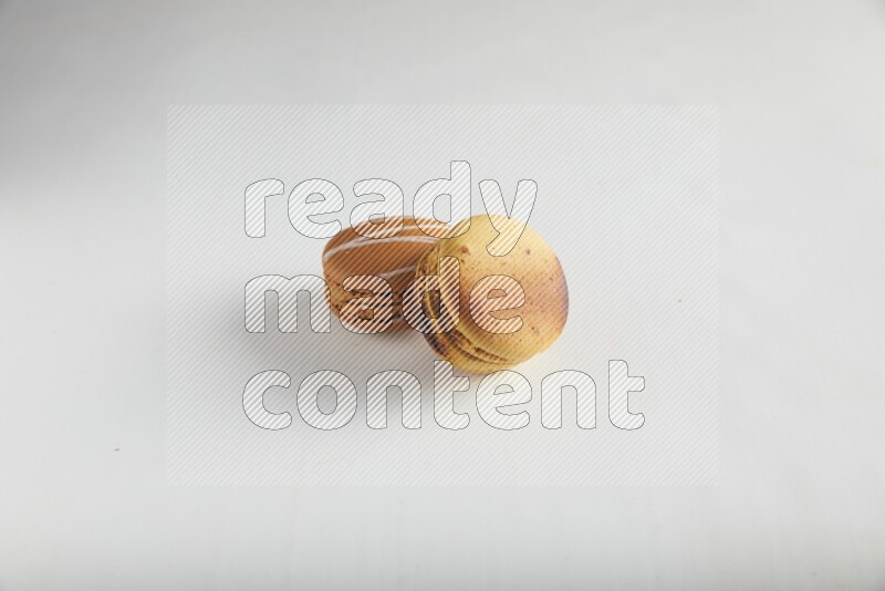 45º Shot of of two assorted Brown Irish Cream, and Yellow Crème Brulée macarons on white background