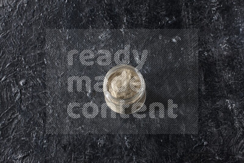 A glass jar full of white pepper powder on textured black flooring