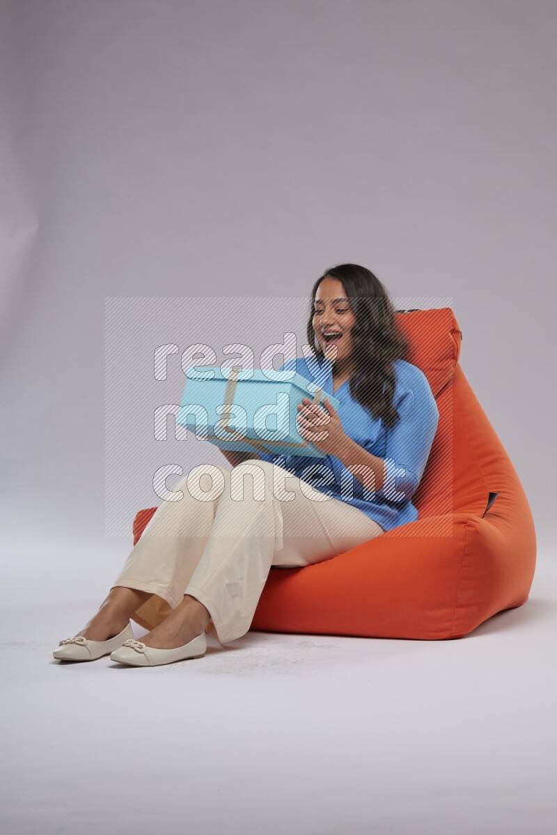 A woman sitting on an orange beanbag and opining a gift