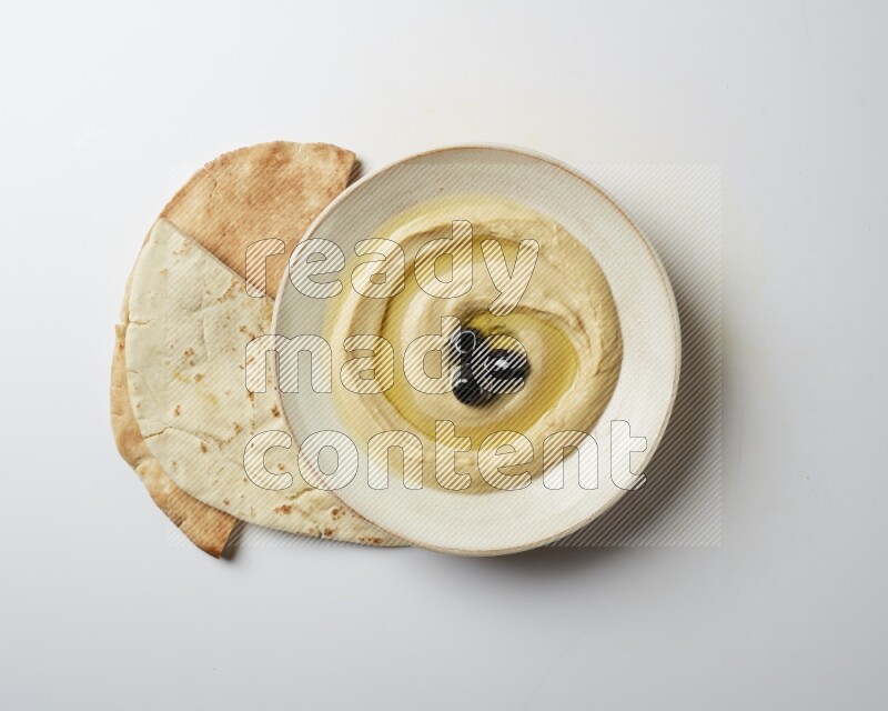 Hummus in a pottry plate garnished with black olives on a white background