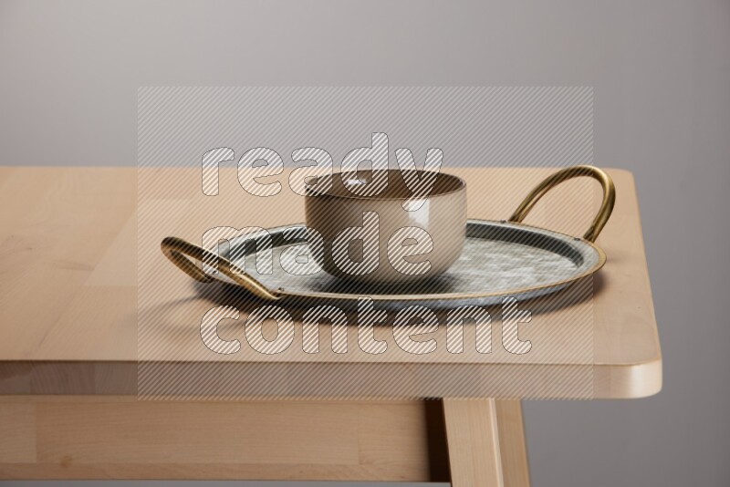multicolored bowl placed on a rounded stainless steel tray with golden handels on the edge of wooden table