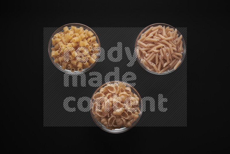 Different pasta types in glass bowls on black background