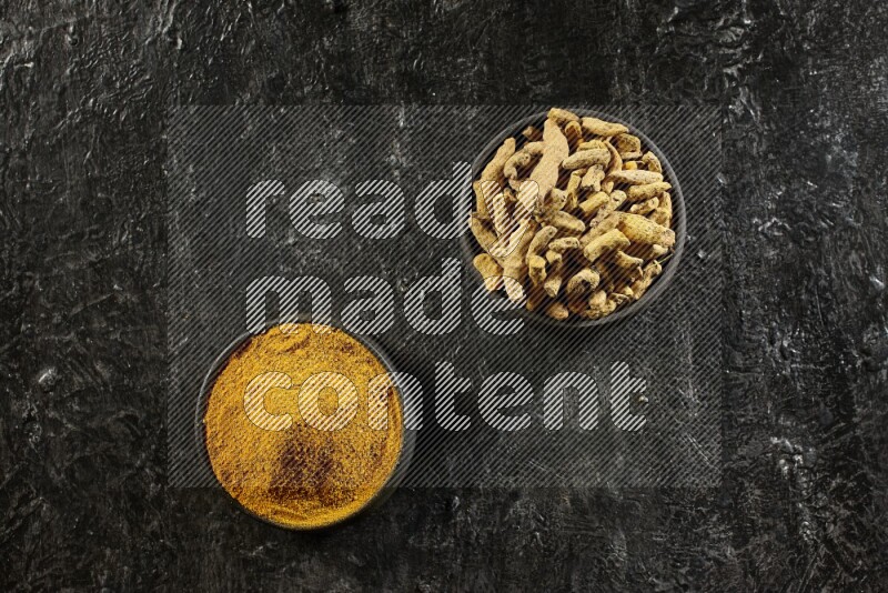 وعاءان من الفخار باللون الأسود، أحدهما ممتلئ ببودرة الكركم والآخر ممتلئ بأصابع كاملة من الكركم المجفف على خلفية سوداء