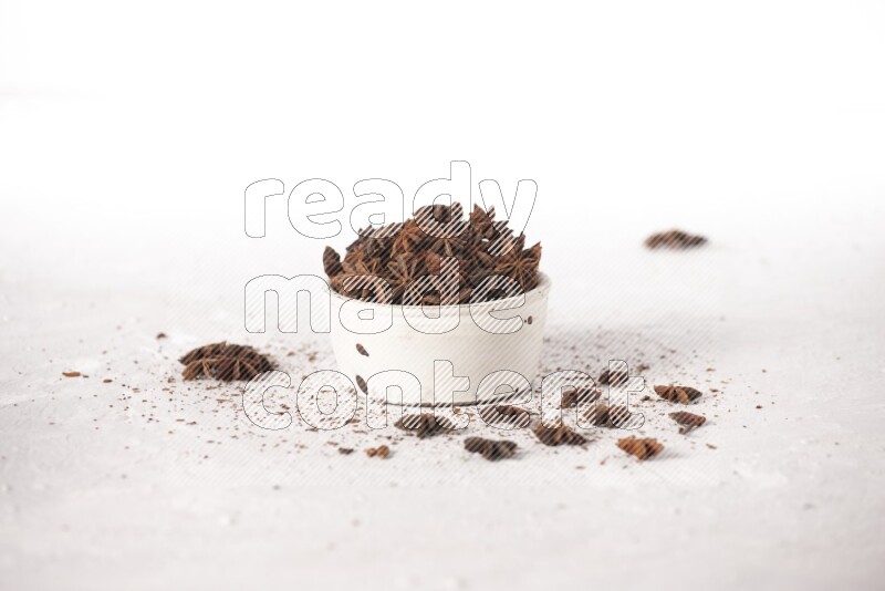 Star Anise in a white bowl and more of it sprinkled on white background