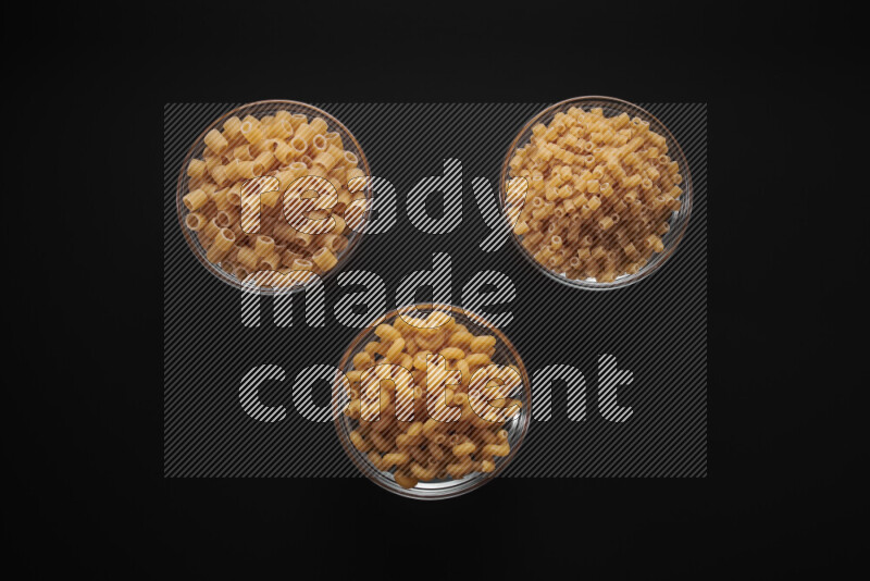 Different pasta types in glass bowls on black background