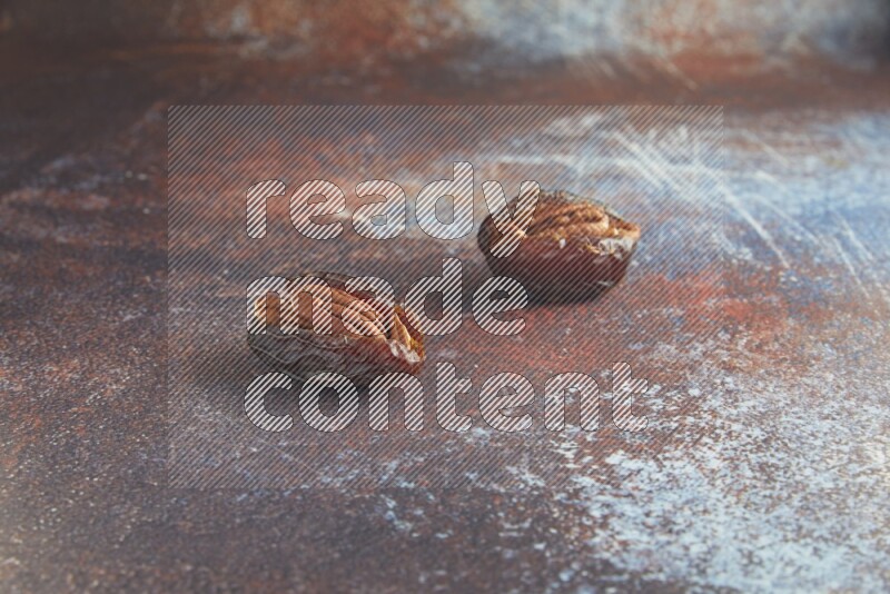 two pecan stuffed madjoul dates on a rustic reddish background