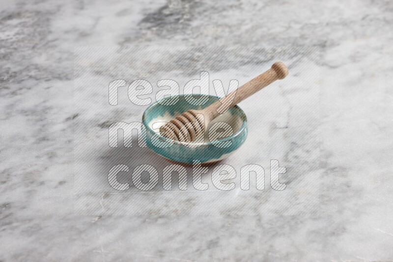 Multicolored pottery bowl with wooden honey dipper in it on grey marble background