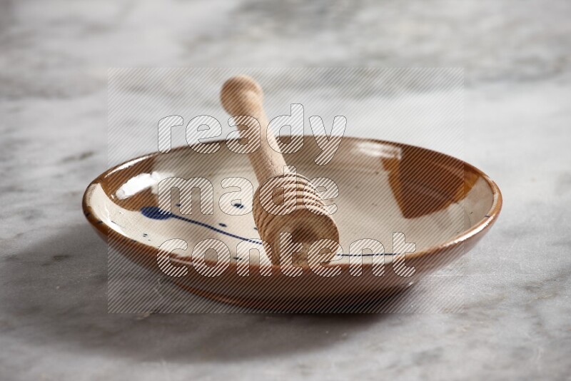 Multicolored pottery plate with wooden honey dipper in it on grey marble background