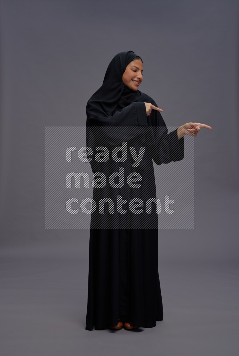 Saudi woman wearing Abaya standing interacting with the camera on gray background