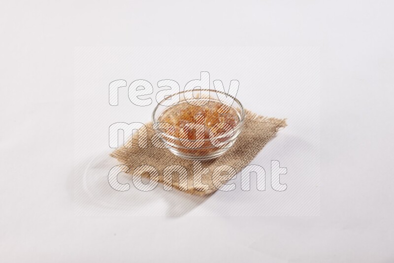A glass bowl full of gum arabic on a burlap piece on white flooring