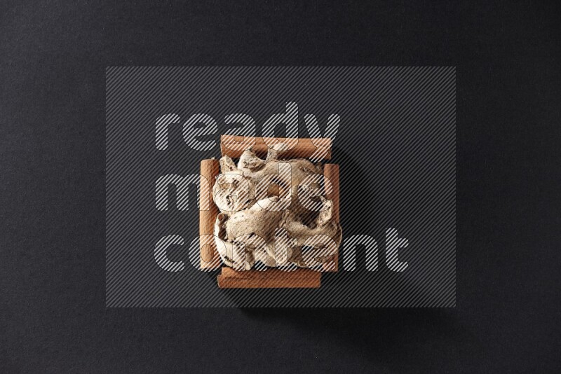 أربعة من أعواد القرفة مكونة شكل مربع بداخلها زنجبيل مجفف علي خلفية سوداء