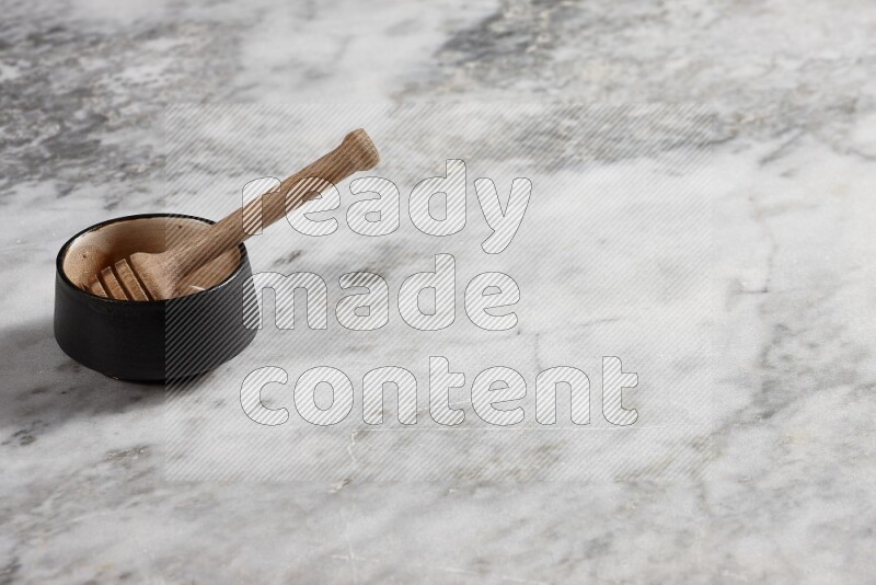 Black pottery bowl with wooden honey dipper in it on grey marble background