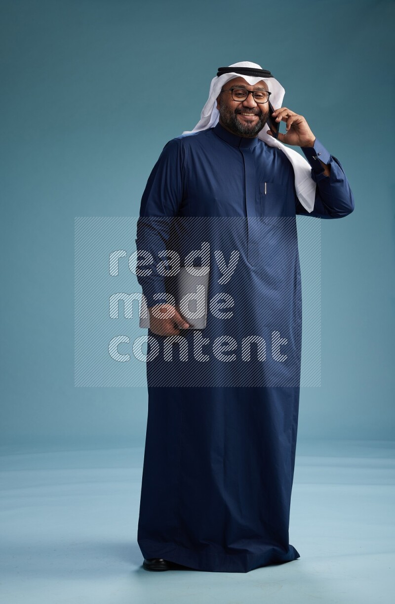 Saudi Man with shimag Standing talking on phone on blue background