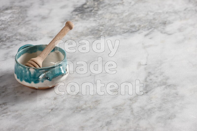 Multicolored pottery bowl with wooden honey dipper in it on grey marble background