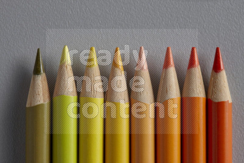 A collection of sharpened colored pencils arranged showcasing a gradient of yellow and orange hues on grey background