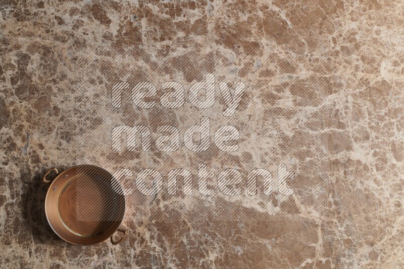 A small copper pan on beige marble background