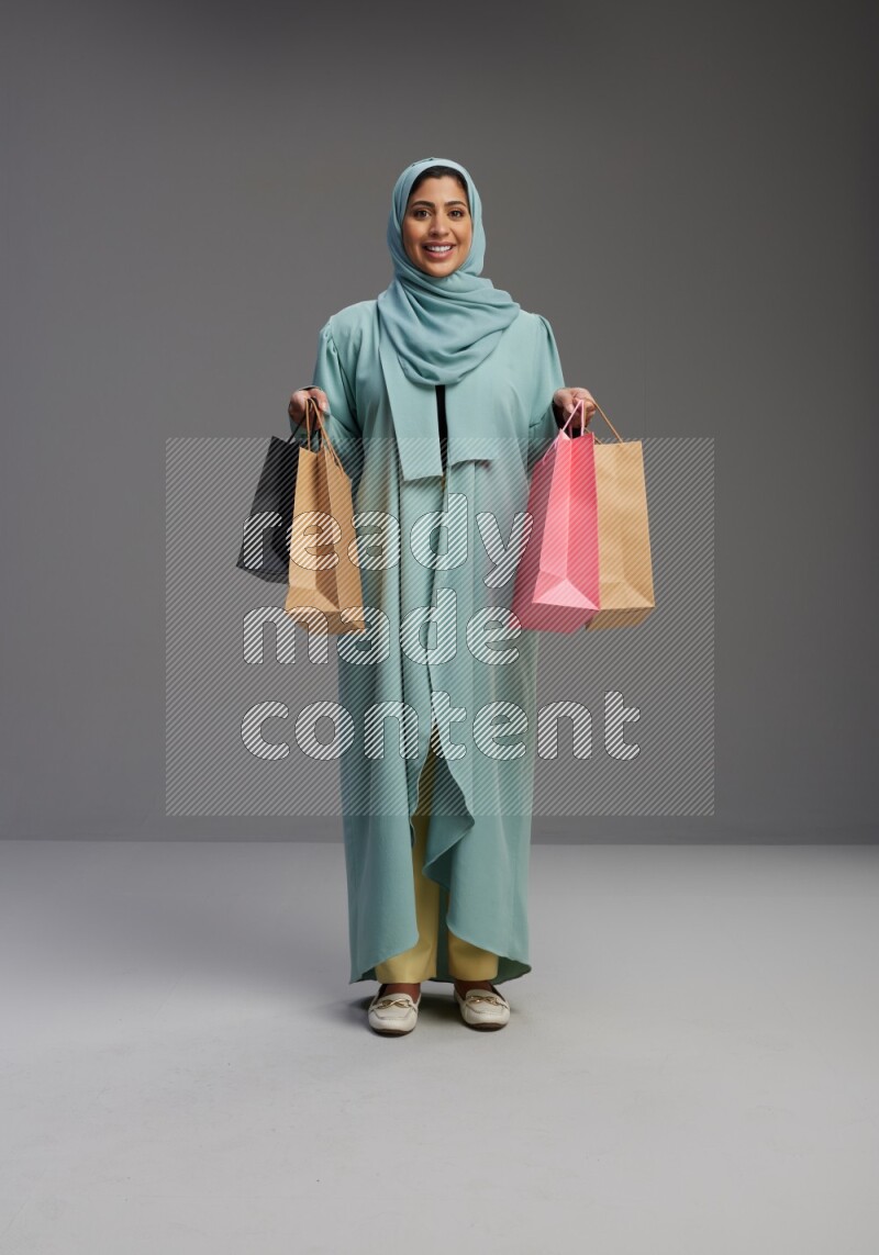 Saudi Woman wearing Abaya standing holding shopping bag on Gray background