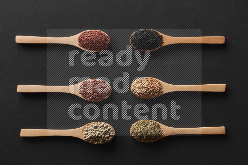 wooden spoons filled with white peppers, mustard seeds, black seeds, garden cress, cumin and flax on black flooring