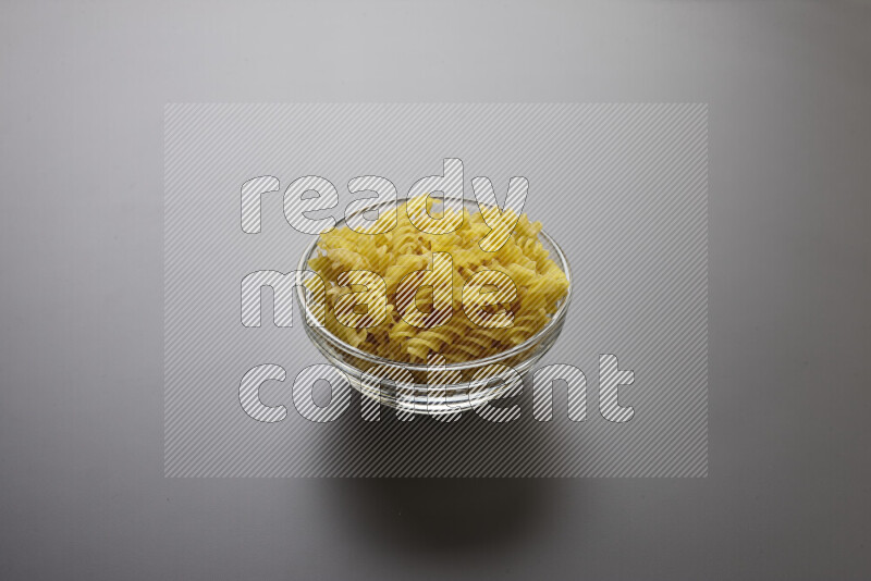Fusilli pasta in a glass bowl on grey background