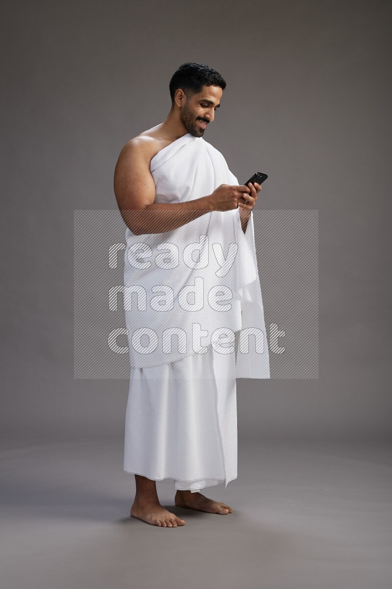 A man wearing Ehram Standing texting on phone on gray background