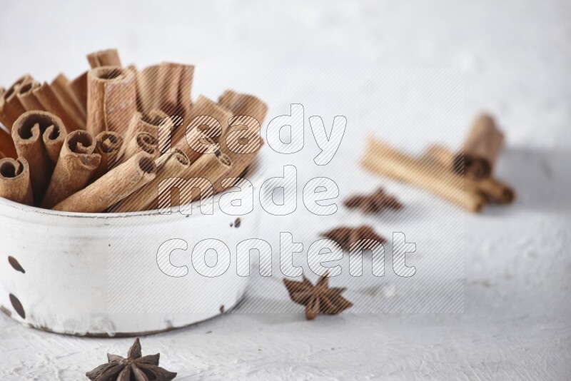 White bowl full of cinnamon sticks surrounded by star anis on a textured white background in different angles