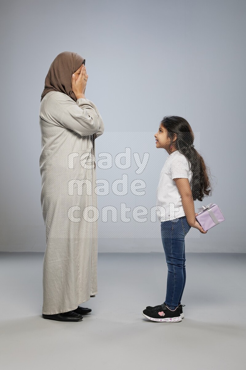 A girl standing hiding a gift behind her back for her mother on gray background