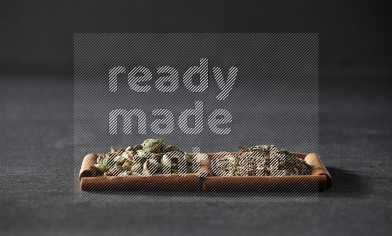 مربعان من أعواد القرفة ممتلئان بحبوب الكمون وحبوب الهيل علي خلفية سوداء