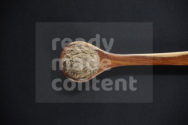 A wooden ladle full of cardamom powder on black flooring