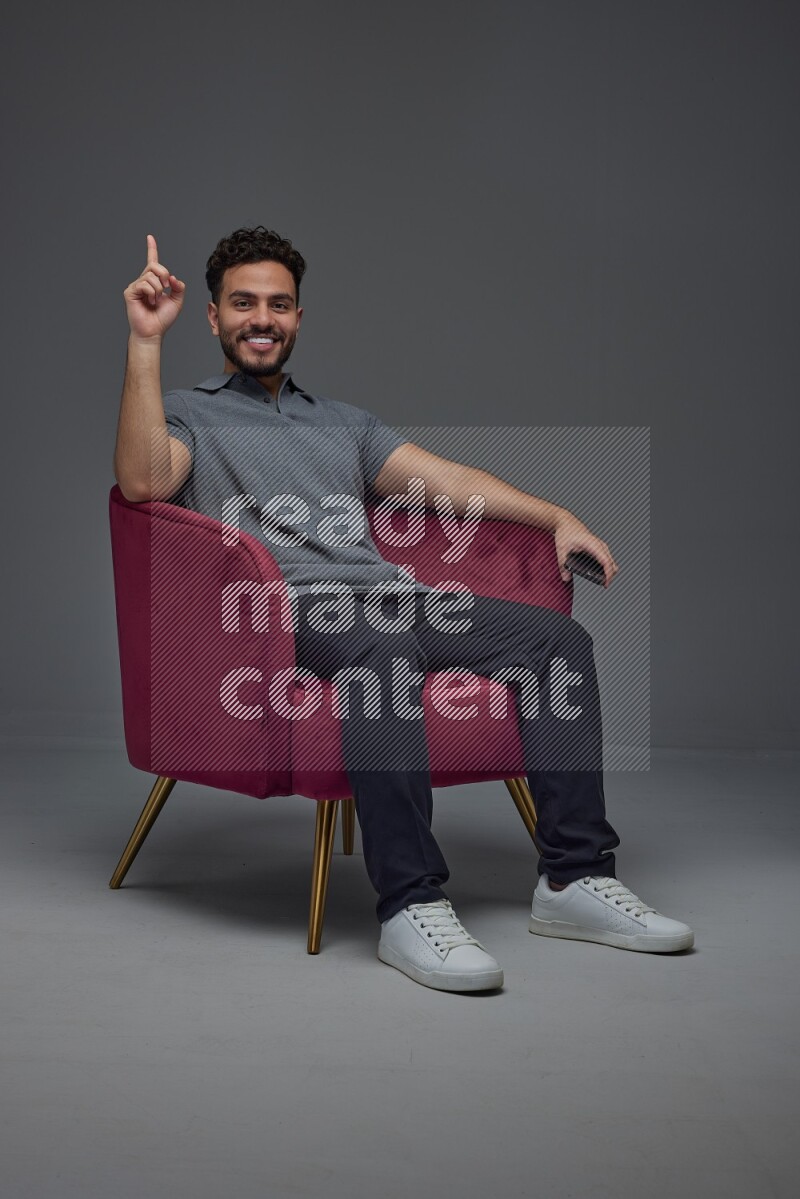 A man wearing casual talking in the phone and making multi hand gestures while sitting on a burgundy chair different angles eye level on a gray background