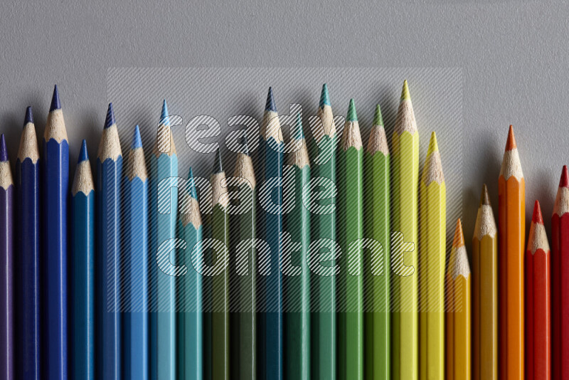 A collection of colored pencils arranged showcasing a gradient of different hues on grey background