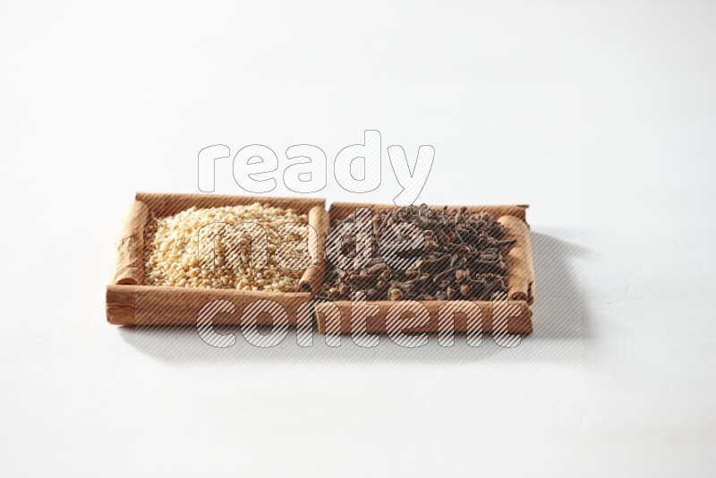 مربعان من أعواد القرفة ممتلئان بالقرنفل وبذور السمسم علي خلفية بيضاء