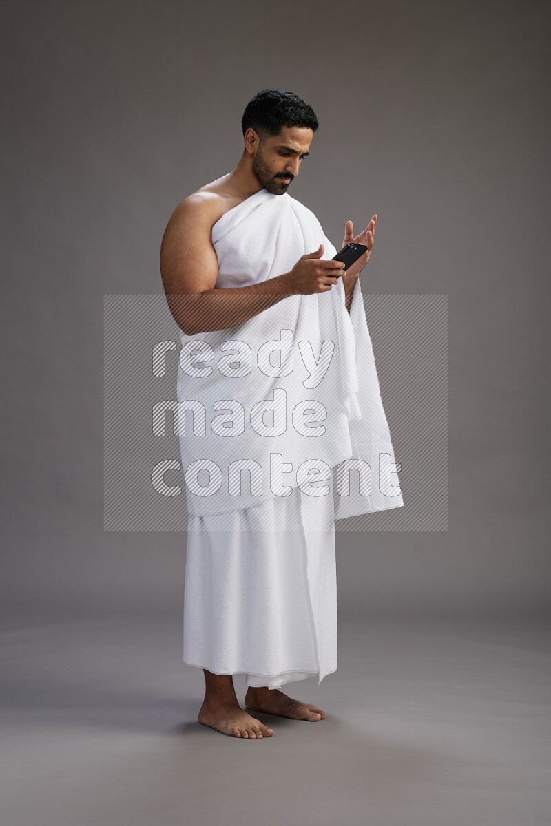 A man wearing Ehram Standing texting on phone on gray background