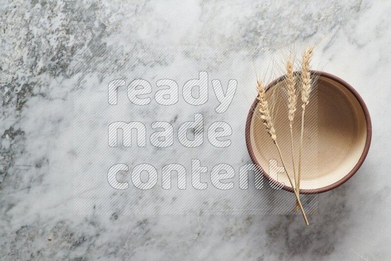 Wheat stalks on beige pottery oven bowl on grey marble background