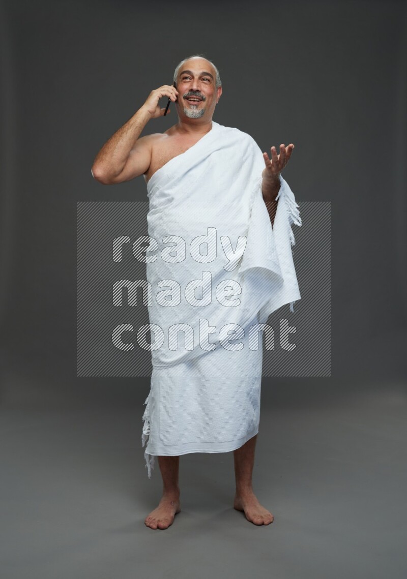 A man wearing Ehram Standing talking on phone on gray background