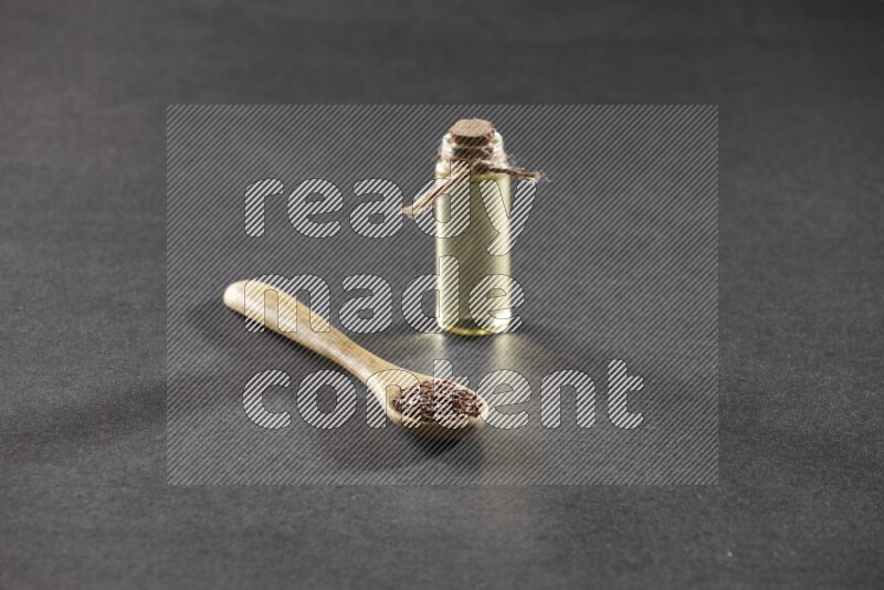 A wooden spoon full of flaxseeds with a glass bottle of flaxseeds oil on a black flooring