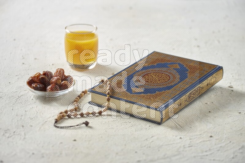 Quran with dates, prayer beads and different drinks all placed on textured white background