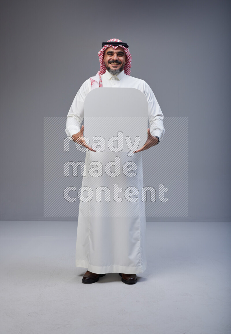 Saudi man Wearing Thob and red Shomag standing holding social media sign on Gray background