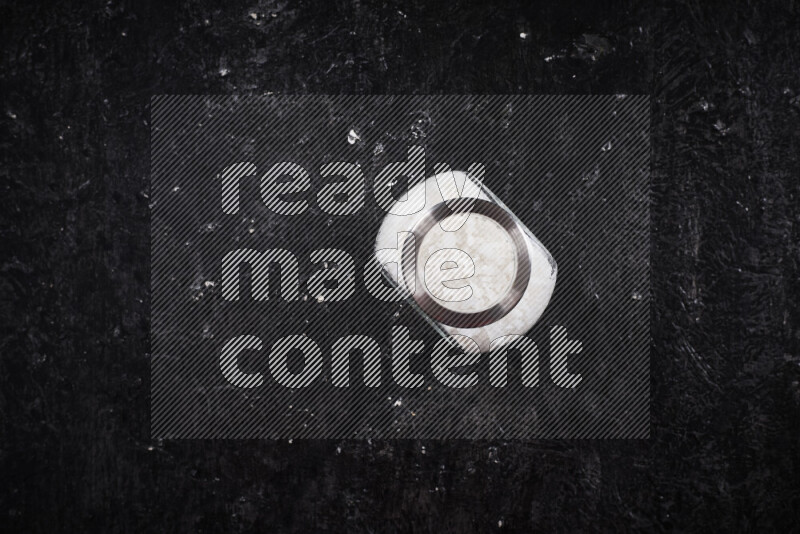 A glass jar full of coarse sea salt crystals on black background