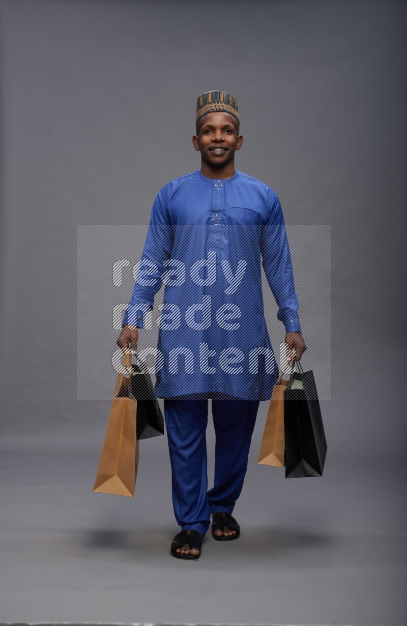 Man wearing Nigerian outfit standing holding shopping bag on gray background